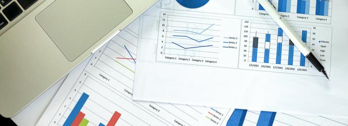 Paperwork with charts and graphs on a table with a laptop