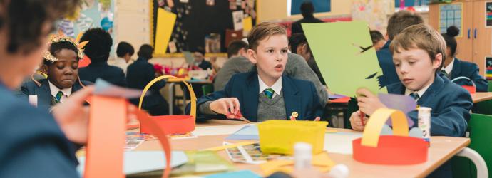 Image shows children of primary school age cutting up coloured card to make head dresses