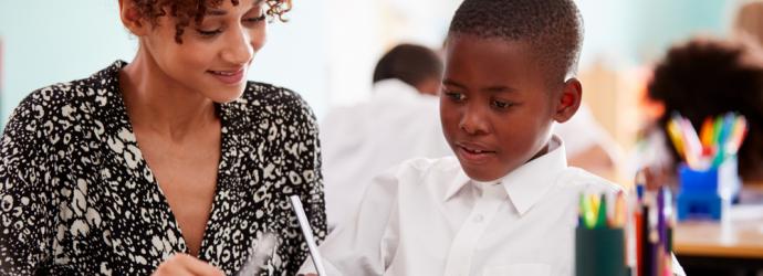 Female teacher providing teaching support for young male pupil - primary