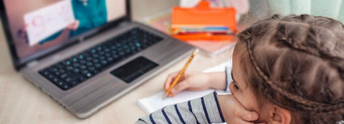 image shows a young child being home schooled over a laptop device