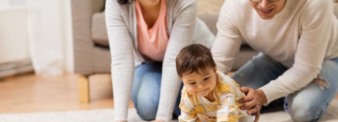Two parents crawling on floor with baby