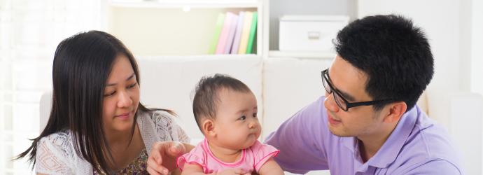 An image of a mom and a dad looking at their baby who is wearing a pink dress