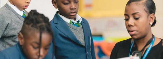 Image shows a teacher helping primary aged children read through some instructions for an activity