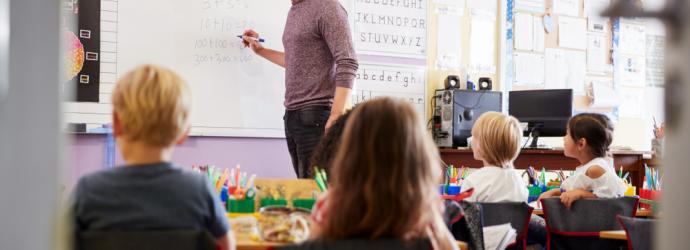 Male teacher writing on a white board in front of primary school children