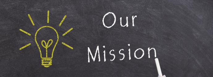 Our mission written on a chalkboard in white alongside a yellow light bulb also written on the chalk board