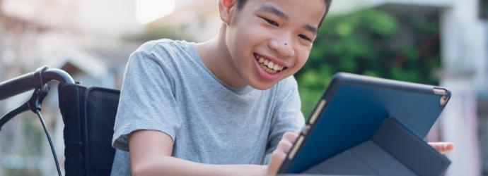 boy sitting in a wheelchair watching a tablet device