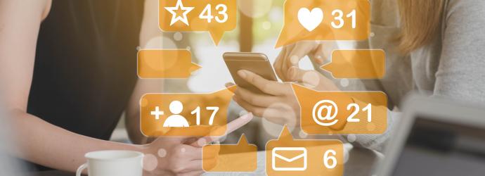 Two women having coffee with their mobile devices. A group of social media icons in Yellow appear to be bursting out of the devices