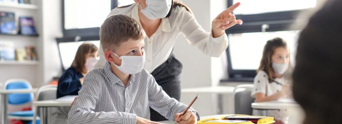 Female teacher supporting male pupil - both are wearing masks in the classroom