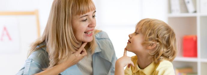 Female teacher with young boy supporting with speech language and communication needs at a table in a classroom