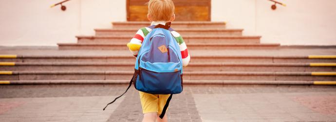 Young boy with a back-back on walking towards school doors that are at the top of a set of wide stairs