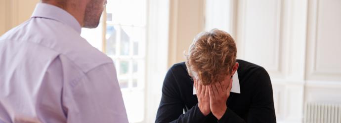 Young male with head in hands with a teacher who is supporting him