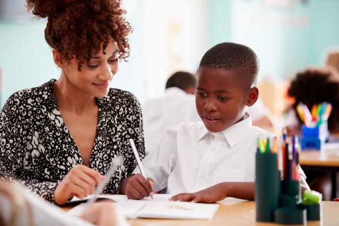 Female teacher providing teaching support for young male pupil - primary