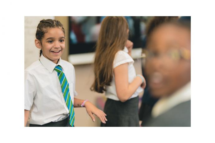 Image shows primary aged pupils walking around their classroom and laughing.