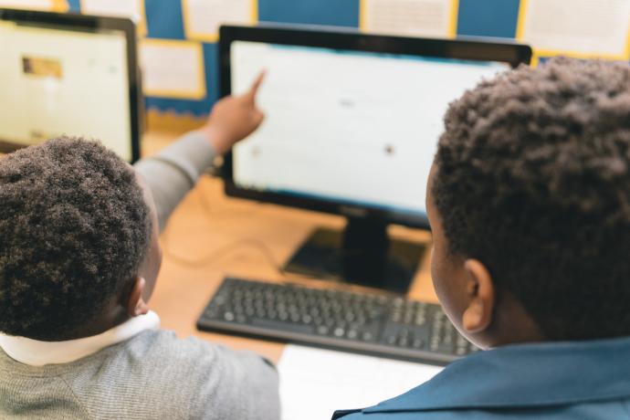 Image shows two pupils using a computer, with one pointing at the screen