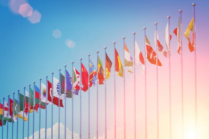 Image of flag poles with multiple countries flags with a bright blue sky in the background