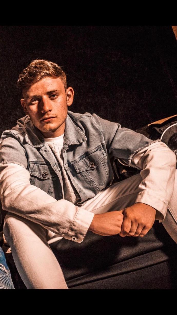 Photograph of Jack Grange wearing a denim jacket sitting on a chair