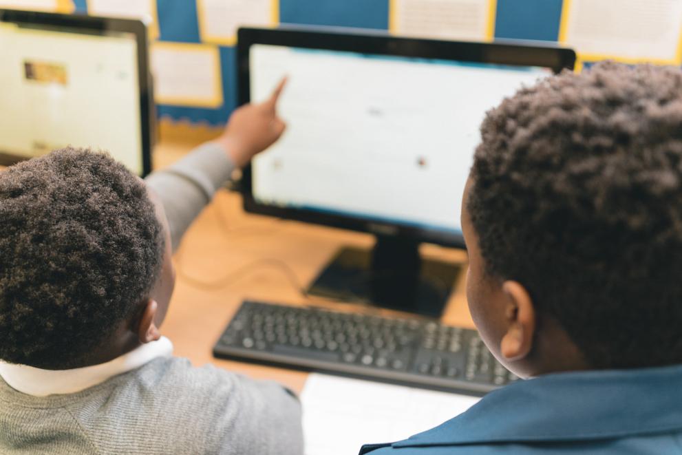 Image shows two pupils using a computer, with one pointing at the screen